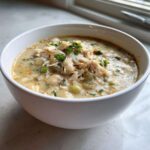 A close-up of a creamy white chicken chili recipe, topped with shredded chicken and fresh parsley.
