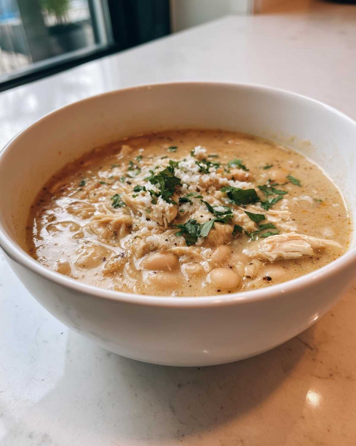A close-up of a creamy white chicken chili recipe, topped with crumbled cheese and fresh cilantro.