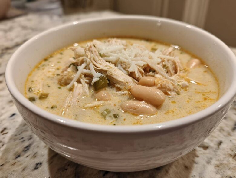 A close-up of a white bowl filled with creamy white chicken chili recipe, topped with shredded cheese.