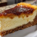 A close-up slice of creme brulee cheesecake featuring a creamy center and a dark, caramelized, torched sugar topping.
