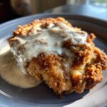 A close-up of a perfectly golden, crispy chicken fried steak smothered in white peppered gravy.