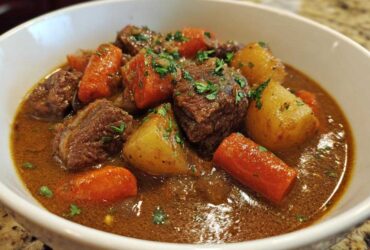 Close-up of a white bowl filled with rich crockpot beef stew featuring tender beef chunks, carrots, and potatoes, garnished with parsley.