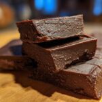 A stack of rich, dark chocolate fudge pieces resting on a wooden surface, showcasing the texture of the easy fudge.