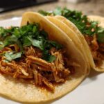 Close-up of three soft corn tortillas filled with saucy shredded chicken and topped generously with fresh cilantro for easy chicken tacos.