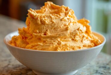 A close-up of bright orange, fluffy pumpkin fluff dessert piled high in a white serving bowl.