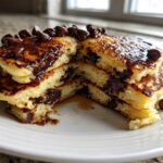 Close-up of a stack of fluffy chocolate chip pancakes cut open to show melted chips and syrup.