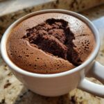 Close-up of light and airy chocolate mousse served in a white mug, showing bubbly texture.