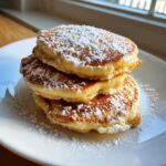 A stack of three fluffy discard pancakes generously dusted with white powdered sugar on a white plate.