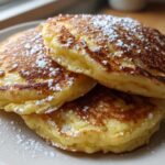A stack of three incredibly fluffy discard pancakes, perfectly golden brown and dusted generously with powdered sugar.
