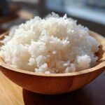 Close-up of perfectly cooked, fluffy white sushi rice mounded high in a light wooden bowl.