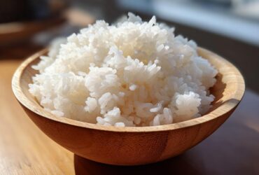 Close-up of perfectly cooked, fluffy white sushi rice mounded high in a light wooden bowl.