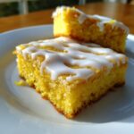 Close-up of two fudgy lemon brownies stacked on a white plate, topped with thick white lemon glaze.