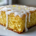 A close-up of a single square of fudgy lemon brownies topped with thick, dripping white glaze and lemon zest.