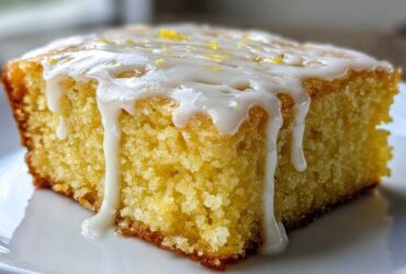 A close-up of a single square of fudgy lemon brownies topped with thick, dripping white glaze and lemon zest.