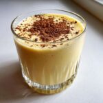 A glass filled with creamy homemade eggnog, topped generously with freshly grated cocoa powder.