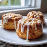 Three golden baked apple fritters drizzled heavily with white vanilla glaze, sitting on a white plate.