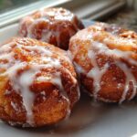 Three golden brown baked apple fritters generously drizzled with white vanilla glaze, sitting on a white plate.