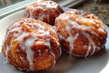 Three golden brown baked apple fritters generously drizzled with white vanilla glaze, sitting on a white plate.