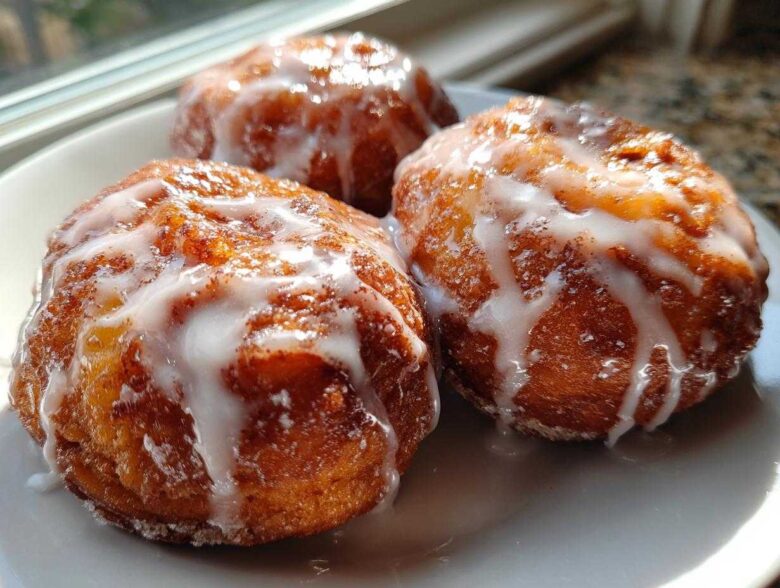 Three golden brown baked apple fritters generously drizzled with white vanilla glaze, sitting on a white plate.