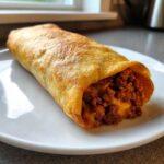 A crispy, golden-brown chimichangas filled with seasoned ground beef and melted cheese, served on a white plate.