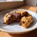 Close-up of a warm, gooey vegan chocolate chip cookie broken in half, showing melted chocolate.
