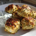 A plate of golden brown greek chicken meatballs served with a side of creamy tzatziki sauce.