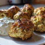 Close-up of golden brown greek chicken meatballs served on a white plate next to a dollop of creamy tzatziki sauce.