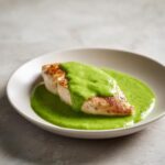 A perfectly cooked piece of grilled chicken breast topped generously with vibrant green cilantro lime sauce.
