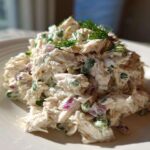 A mound of creamy cottage cheese chicken salad mixed with red onion and green herbs, garnished with dill.