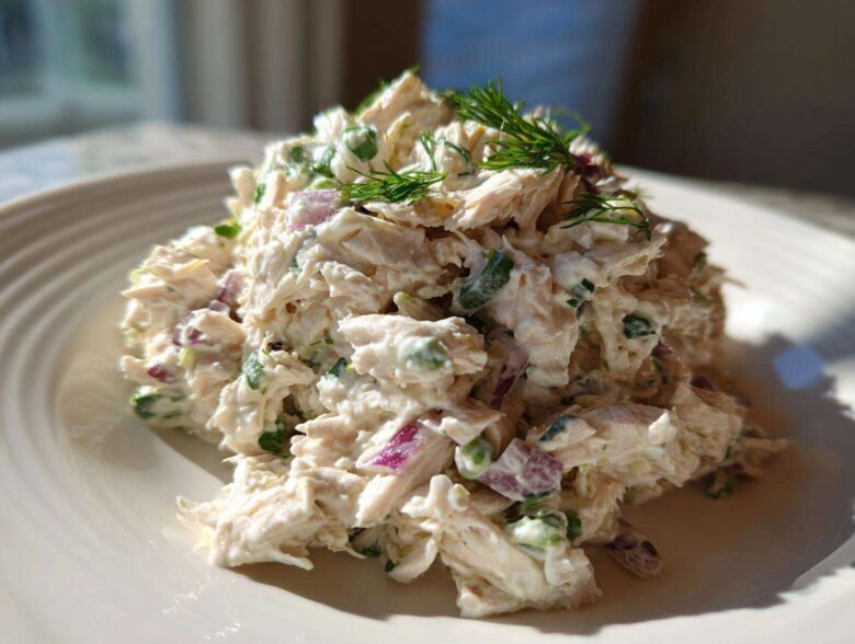 A mound of creamy cottage cheese chicken salad mixed with red onion and green herbs, garnished with dill.