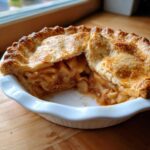 A close-up view of a homemade apple pie with a slice removed, showing caramelized apple filling and a flaky, golden crust.