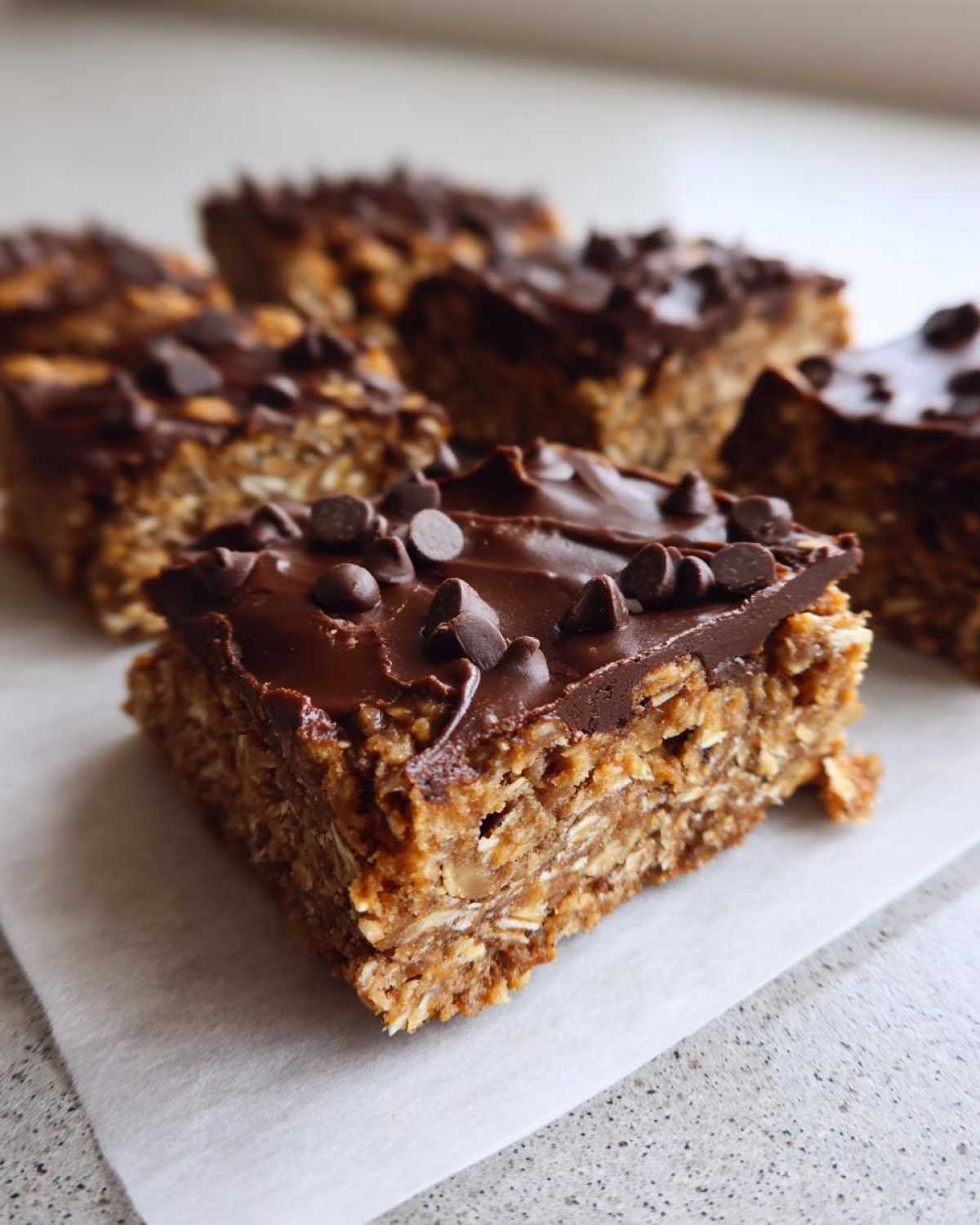 A close-up of a homemade protein bars square topped with melted chocolate and mini chocolate chips.