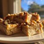 A stack of rich, creamy maple fudge squares topped with chopped pecans, beautifully lit by sunlight.