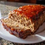 Close-up of a juicy meatloaf, sliced and topped with a thick, shiny orange glaze.
