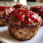 Close-up of several baked mini meatloaf portions topped with a shiny red ketchup glaze.