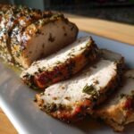 Slices of juicy slow cooker turkey breast coated in herbs and spices, resting on a white platter.