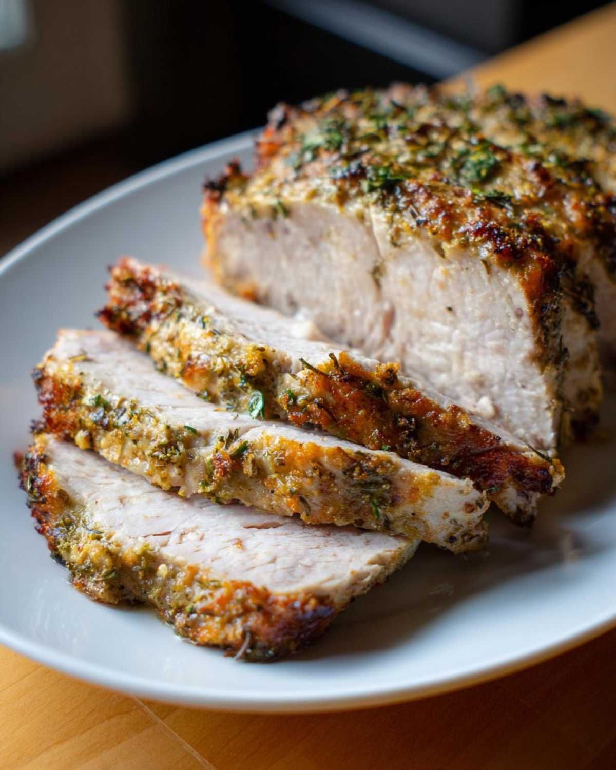 Close-up of sliced, juicy slow cooker turkey breast with a browned, herbed crust on a white plate.