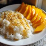 A plate of sweet mango sticky rice topped with golden syrup and toasted sesame seeds.