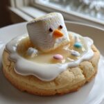 A single melted snowman cookie featuring a marshmallow head sinking into white icing, with candy buttons, set against a bright window background.