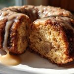 A slice cut from a moist apple bundt cake, drizzled heavily with a thick caramel glaze.
