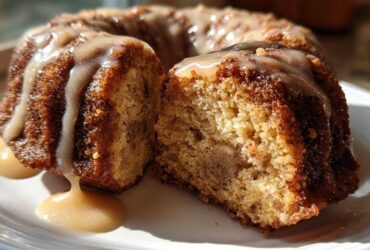 A slice cut from a moist apple bundt cake, drizzled heavily with a thick caramel glaze.