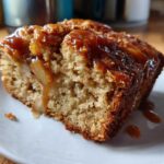Close-up of a moist slice of apple dapple cake topped with gooey caramel sauce dripping down the side.