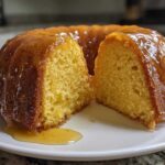 A golden, moist Bacardi Rum Cake, drizzled heavily with glaze, sliced in half on a white plate.