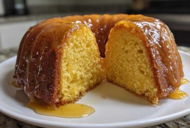 A golden, moist Bacardi Rum Cake, drizzled heavily with glaze, sliced in half on a white plate.