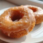 Two moist baked pumpkin donuts covered in a thick, speckled glaze, resting on a white plate.