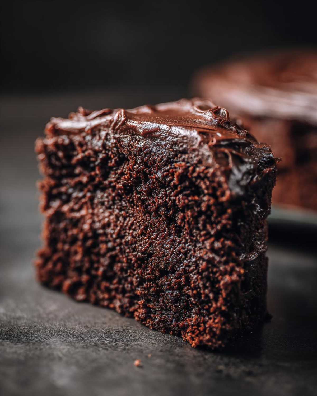 Close-up of a moist slice of dark chocolate cake with glossy frosting, part of the chocolate cake recipe.