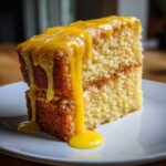 Close-up of a moist, two-layer lemon cake recipe slice topped with thick, dripping yellow lemon glaze.