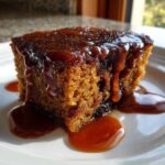 A close-up of a moist slice of sticky toffee pudding generously covered in rich toffee sauce.