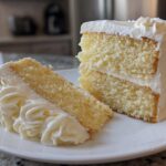 Two slices of moist vanilla cake recipe with thick white buttercream frosting on a white plate.
