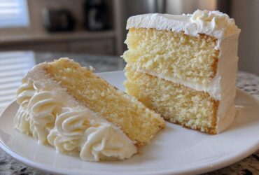 Two slices of moist vanilla cake recipe with thick white buttercream frosting on a white plate.